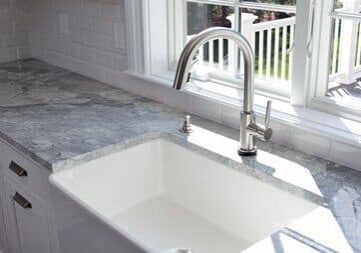 Modern kitchen sink and single handle brass faucet with soap dispenser, marble countertop and window to the garden.